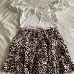 Ribbad vit magtröja i polyester med rosett vid brösten. En leopardmönstrad kjol i polyester med volanger. Båda är i L med känns som medium.