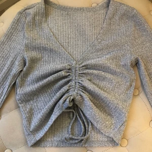 Topp - Ljusgrå tröja med ett snöre som man kan ändra längden på tröjan med. Aldrig använt. Frakt betalas av köparen.