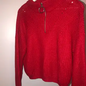 En röd stickad tröja med en drag kedja vid halsen som går att dra ner och upp. Tröjan är andvänd två gånger och har legat i en garderob i två år helt orörd, så den är i ett bra skick.