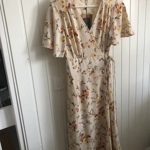 Ny Vero Moda klänning  - Ny klänning med beige botten och blommor. Vadlång i storlek S. Fin omlott med snörning i midjan. 