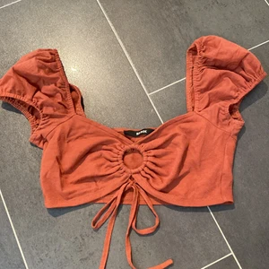 Topp - En rödbrun topp från bikbok som har en öppen ring i mitten med snöre som man kan knyta en fin rosett med! Aldrig använd då den var för liten!
