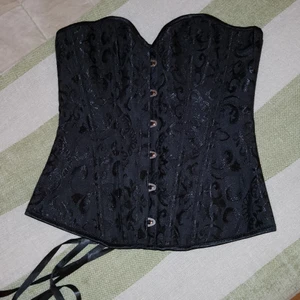 Korsett (Oanvänd) Stl. S - Helt oanvänd korsett i stl S. Första bilden framsidan, andra bilden baksidan och tredje på insidan. Använt blixt på andra bilden för att förtydliga mönstren som är i sammetsliknande material. Korsetten är annars helt svart (med mönster). Kan skicka fler bilder vid efterfrågan. Kan mötas upp i Göteborg eller skickas mot att köpare betalar frakt. 🥰