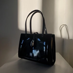 Vinylväska - Söt liten väska i vinyl som glänser fint i solen. Många hårda fack inuti och bra och rubust kvalité både inne och utanpå. Begagnat skick med några repor och liknande. 