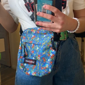  Axelremsväska Eastpak - Ljusblå,Fint blommigt mönster, Skick 10/10 då den aldrig är använd.  En ytterficka bak, samt en till ficka innuti. 