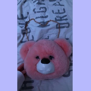Björnväska - Rosa fluffig nallebjörnsväska som har en guldig dragkedja och guldig kedja som handtag. Man kan knäppa lös handtaget och göra om det till en ryggsäck om man vill det. Den får plats med ganska mycket för att vara så liten. Säljer den för 100kr plus frakt som ligger på 66kr. Bara att höra av sig om man har frågor🫀