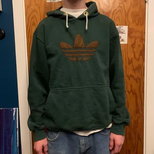 Adidas Hoodie (Vintage) grön - Mörkgrön Vintage Adidas Hoodie (M). Köpt på secondhand för ett år sedan men passar inte min stil längre. Finns ingen storlek på tröjan men skulle gissa på Medium. (passar mig bra som är 182cm) Har bytt ut snörena för ansåg att originalen var för tjocka. Originalsnörena medföljs också! Den gröna färgen är smått urtvättad, men inte mer än vad som visas på bild:) Bra skick
