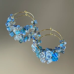 Örhängen  - Handgjorda örhängen med blå glaspärlor i olika storlekar och nyanser fastvirade med guldig ståltråd. Ca 4 cm i diameter. Säljs separat för 100kr, 2 par för 175kr ✨❣️  ************************** Checka min profil där jag har en massa mer smycken utlagda!! Finns i flera färger och modeller:) Frakt ingår i priset, perfekta för dig som vill sätta en personlig prägel på stilen eller att ge bort i present ❤️‍🔥puss❤️‍🔥