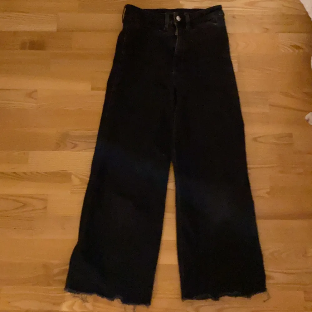 Ett par svarta högmidjade jeans med fransar längst ner. Jeans & Byxor.