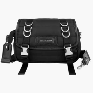 Ideal of Sweden väska helt ny - Tillverkad av 100 % återvunnen polyester Mått: 22 cm övre bredd x 22 cm nedre bredd x 6 cm djup x 15 cm höjd Silverfärgade metalldetaljer och kraftig kedja En justerbar och avtagbar rem medföljer som mäter 83 cm–130 cm Kompatibel med våra remmar Kan bäras som en clutch eller som en crossbody bag. Ny pris 999kr