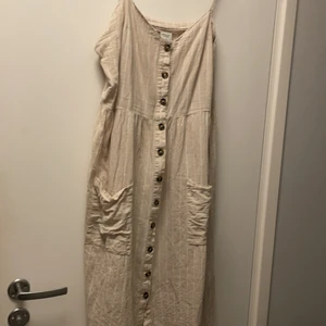 Fin klänning i storlek 42 - Jättesöt klänning som är beigevit randig, knälång med knappar fram hela vägen ner. Ifrån jacqueline de yong. Använd men fortfarande i fint skick! Fickor fram. Nästan som linnetyg. Köparen står för frakt