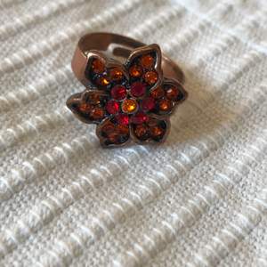 Jättefin ring med en blomma som har röda och orangea stenar/paljetter! Den är även reglerbar så den passar alla🥰 Nickelfri - 10kr || köpare står för 12kr frakt