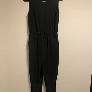 Jumpsuit - En svart jumpsuit med omlottrygg och snygga detaljer på axlarna samt fickor på benen.