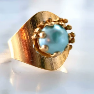 Guldfärgad ring med blå pärla - Guldfärgad ring med blå pärla. Supercool att ha med ett par mindre guldfärgaderingar.😇Kontakta vid intresse.