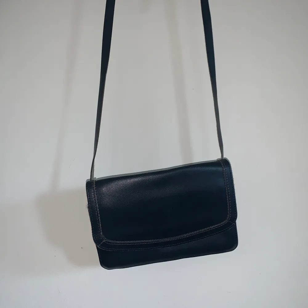 Mörkblå (färgen är svår att se på bilden) handväska med långt, justerbart axelband. Tre fack innuti, ett med dragkedja. Mått: 20x14x4 cm (djupet går att förstora) Axelbandets mått: va 110cm🌟. Väskor.