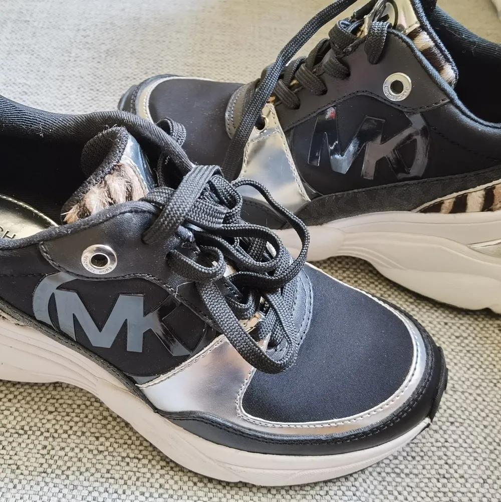 Michael Kors sneakers i storlek 36, endast använda ett fåtal gånger, inköpta på Zalando, nypris 2800 kronor, inga defekter, inbyggd kilklack, dom är svarta med vit sula, silverfärgade detaljer, logga både på sidan och i bak, flärpen och sidorna är mönstrad i leopard mönster, finns i Kallebäck eller kn skickas spårbart om köpare står för frakt på 99 kronor. . Skor.