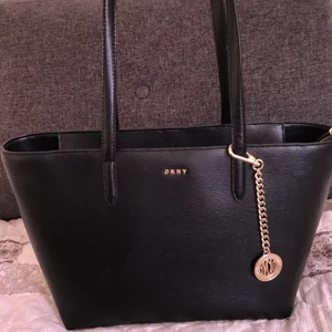 DKNY handväska - En fin handväska från DKNY. Den är varken för ator eller för liten. Materialet är 100% koläder. Jag köote den förra sommaren för 2045kr. Den är knappt använd så därför säkjer jag den för 1400kr, pris kan diskuteras vid snabbt köp.