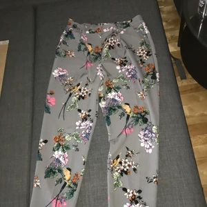 kostymbyxor i kreativt tema från soaked  - gråa kostymbyxor med mönster av blommor och fåglar från soaked. storleken är m, men midjan är stretchig. framfickor samt fejkade bakfickor. har använts endast en gång. priset är allt som allt 316 kr (priset på byxorna + frakten).