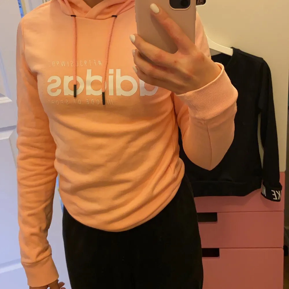 Aprikos adidas hoodie som sitter ganska tajt men lång i ärmarna. På hoodien så står det junior xxs. Men jag bär annars i vanlig storlek xs, och den här hoodien passar på mig. Men säljer för att den ej kommer till andvändning. Hoodien är i bra skick och andvänd några få gånger.  Runt 50/60kr.. Hoodies.