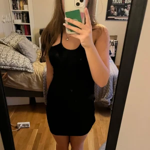 Svart kortklänning - Säljer en stilren svart kortklänning som är perfekt för fest. Klänningen är ärmlös med smala axelband och har en tight passform. Den är gjord i ett mjukt och bekvämt material, vilket gör den både snygg och skön att bära.