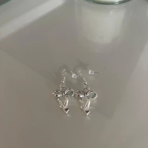 Snygga silverörhängen med rosett - Säljer ett par superfina örhängen i silverfärg med en elegant rosettform. Perfekta för att ge en extra touch till din outfit, oavsett om det är till vardags eller fest. De är lätta och bekväma att bära hela dagen.