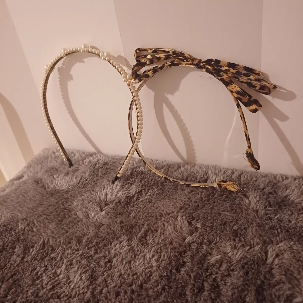 Två snygga diadem till salu! Det ena är täckt med vita pärlor som ger en elegant touch, perfekt för festliga tillfällen. Det andra har ett coolt leopardmönster och en söt rosett på toppen, vilket ger en trendig och djärv look. . Accessoarer.