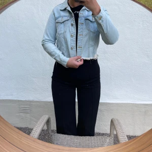 Ljusblå croppad jeansjacka - Säljer en snygg ljusblå croppad jeansjacka med knappar framtill. Jackan har en klassisk krage och två bröstfickor med knappdetaljer. Perfekt för vår och sommar, och ger en cool touch till vilken outfit som helst!