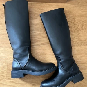 Knähöga boots - Svarta knähöga boots/stövlar. Använda ett fåtal gång och är i väldigt fint skick. Dragkedja på insidan. Strl 36