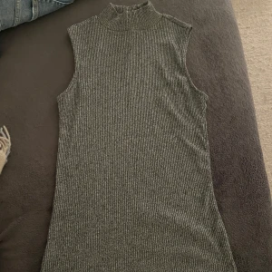 Grå ribbad ärmlös topp från 157 - Säljer en stilren grå ribbad topp från 157 i storlek M. Den är ärmlös med en hög krage, perfekt för lager-på-lager eller som den är. Toppen är i ett mjukt och stretchigt material som sitter bekvämt. Passar både till vardags och festliga tillfällen.