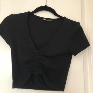 Svart croppad topp från Zara - Snygg svart croppad topp från Zara med korta ärmar och v-ringad. Toppen har en snygg rynkad detalj framtill. 🩷