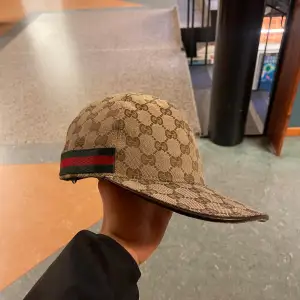 Säljer en snygg beige keps från Gucci med deras ikoniska monogrammönster. Kepsen har en grön och röd randdetalj på sidan och justerbar rem baktill. Perfekt för att ge din outfit en lyxig touch.!     Köptes i 2023 vår kvitto finna måste ba leta fram pris kan diskuteras!!