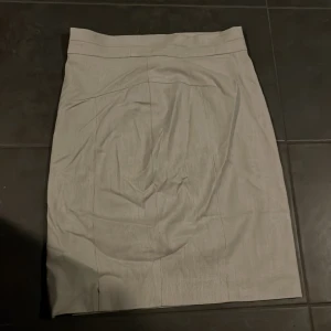 Beige kjol från H&M - Säljer en stilren beige kjol från H&M i storlek M. Kjolen har en klassisk design med en liten slits på baksidan för extra rörelsefrihet. Perfekt för både kontoret och vardagsbruk. Materialet känns bekvämt och lätt, vilket gör den idealisk för vår och sommar.