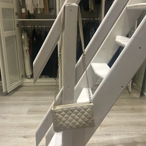 Beige quiltad axelväska - Säljer en superfin beige axelväska med quiltat mönster. Den har en elegant guldkedja som axelrem och en praktisk dragkedja upptill. Perfekt för både vardag och fest! 👜✨