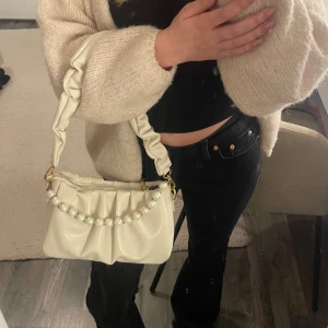 Vit axelväska med pärldetaljer - Säljer en superfin vit axelväska i syntetmaterial. Den har en snygg rynkad design och en axelrem med pärlor som ger en lyxig touch. Väskan är i mycket bra skick och har en avtagbar axelrem. Pärlorna går att ta bort och sätta dit hur man vill❣️💞