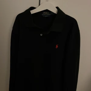 Svart pikétröja från Ralph Lauren - Säljer en stilren svart långärmad pikétröja från Ralph Lauren i slim fit. Tröjan har en klassisk krage och en liten röd broderad logga på bröstet. Perfekt för både vardag och fest! Pris går att diskutera skick är 10/10