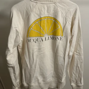 Vit tröja från Acqua Limone - Säljer en snygg vit tröja från Acqua Limone med deras ikoniska gula citrontryck på ryggen och logga på ärmen. Tröjan är i bomull och har en normal passform med ribbade muddar vid ärmslut och nederkant. Perfekt för en avslappnad stil! 🍋