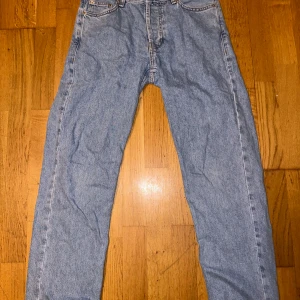 Blå jeansbyxor - Säljer ett par klassiska blå jeansbyxor i bra skick. De har en lite mer baggy/straight passform och är tillverkade i slitstarkt denim. Perfekta för vardagsbruk och kan matchas med nästan vad som helst. De har en traditionell femficksdesign och stängs med dragkedja och knapp.