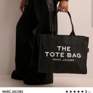 Svart shoppingväska från Marc Jacobs - Snygg och rymlig svart shoppingväska från Marc Jacobs med texten 'THE TOTE BAG' tryckt i vitt. Perfekt för både vardag och shoppingturer. Väskan har två handtag och är tillverkad i ett slitstarkt material.