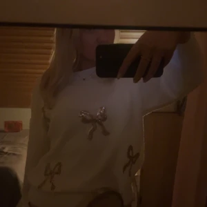 Vit tröja med rosetter - Superfin vit tröja med glittriga rosetter i guld. Perfekt för att liva upp en vardagsoutfit eller till fest. Den är långärmad och ser riktigt mysig ut. Passar bra till både kjol och jeans. Ett måste i garderoben för den som älskar detaljer! ✨