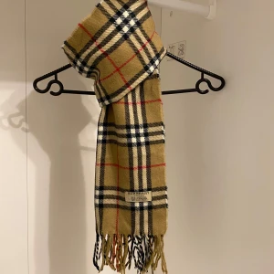 Burberry - Säljer nu denna Snygga halsduk från Burberry i beige.  Tillverkad i mjukt lammull med fransar i ändarna. Perfekt för att hålla dig varm och stilren under kyliga dagar. Den är i mycket fint skick. Hör av dig vid funderingar☺️