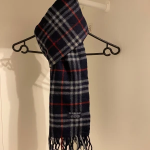 Burberry - Snygg rutig halsduk från Burberry i mörkblått. Tillverkad i 100% mjuk kashmir med klassiska fransar i ändarna. Perfekt för att hålla dig varm och stilren under kyliga dagar. Hör av dig vid funderingar☺️