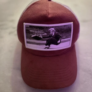 Röd keps med fotoapplikation - Snygg röd keps med vit mesh och en cool fotoapplikation framtill. Märket Unico syns på insidan och sidan av kepsen. Perfekt för en avslappnad stil. Lite missfärgad inuti.