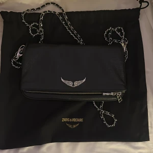 Svart axelväska från Zadig & Voltaire - Snygg svart axelväska i skinn från Zadig & Voltaire med kedjerem och silverdetaljer. Använd fåtal gånger då den inte passade mina guld smycket bra skick, köpt i Köpenhamn 2022.