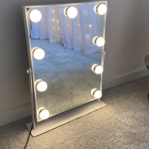 Sminkspegel med lampor - Elegant sminkspegel med inbyggda lampor runt kanterna. Perfekt för att få rätt belysning vid sminkning. Spegeln har en vit ram och står på en stabil bas, vilket gör den enkel att placera på ett bord eller sminkbord. Det finns tre olika lys lägen som går från mindre stark till starkast.                                                  Mått: 30x40 cm