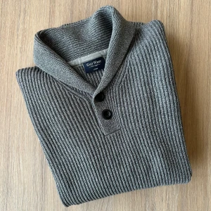 East West ribbstickad 100% bomull, storlek m/l - Snygg grå stickad tröja med krage från East West. Tung och i bra kvalité. Fint skick. Passar mig bra som snarare är medium i storlek så kolla måtten och jämför mot dina tröjor som passar.  100% bomull axelbredd 47 cm, längd 69 cm 