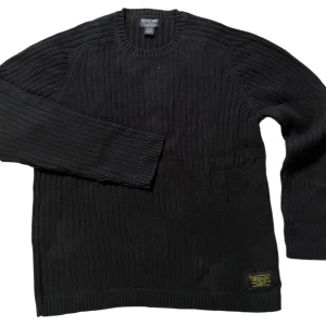 Svart ribbad tröja från Polo Jeans Company - Säljer en svart ribbad tröja från Polo Jeans Company i storlek XL. Tröjan är tillverkad i 100% bomull och har en klassisk rund halsringning. Perfekt för kyligare dagar.