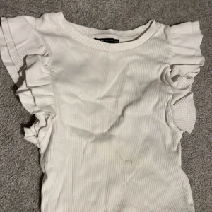 Vit ribbad topp från Zara storlek S - Säljer en söt vit ribbad topp från Zara med volangdetaljer på ärmarna. Storlek S helt okej skick har en fläck(har inte prövat om det går bort i tvätten med fläckborttagning)😊