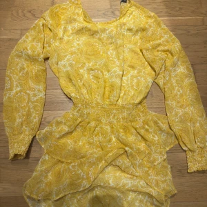 Gul mönstrad klänning från Gina Tricot - Säljer en solig gul klänning från Gina Tricot med ett vackert paisleymönster. Klänningen har långa ärmar och en elastisk midja för en bekväm passform. Perfekt för vår och sommar!