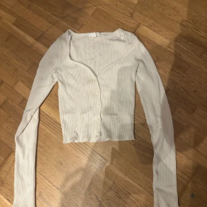 Vit ribbad långärmad topp - Säljer en stilren vit ribbad topp med långa ärmar och knappar framtill. Perfekt för lager-på-lager eller som den är. Passar till många olika outfits!