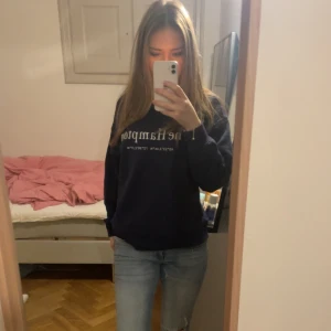 Mörkblå sweatshirt med tryck - Säljer en mörkblå sweatshirt med texten 'The Hamptons' och koordinater tryckta på framsidan. Tröjan har långa ärmar och ribbade muddar vid ärmslut och nederkant. Perfekt för en avslappnad stil. Tröjan är från Gina och är i nyskick. 