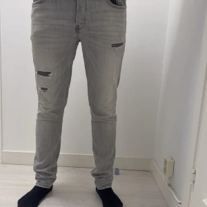 Grå jeans från Dressman - Snygga grå jeans med slitningar på framsidan. De har en klassisk femficksdesign och en bekväm passform. 